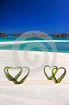 Heart made of palm tree leaves on tropical island with overwater bungalows in the background.