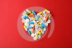 Heart made of pills on red background, space for text