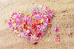 Heart made of pink petals of tropical flowers on the sand, close-up, top view.