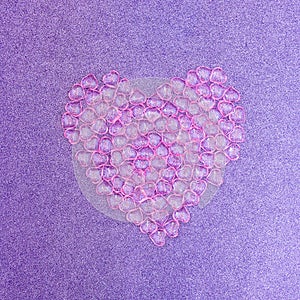 Heart made of pink plastic hearts on a purple glittering background