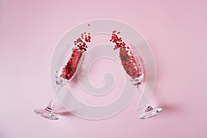 Heart made of pink and red beads pouring out from two transparent wine glasses on the pink background