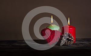 A heart made of red thread, a cone and two lit colored candles