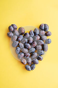 Heart made of ripe plums. Plums on yellow background. Healthy food.