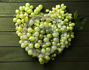 Heart made of ripe sweet grapes on wooden background