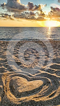 Heart made of sand on beach against background of sea and beautiful sunset in rays of sun, concept of love and health