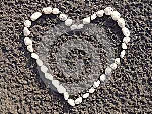 Heart made of small white pebbles on sand closeup