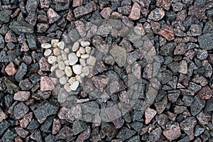 Heart made of small white rounded stones set on background of the gray, pink, and brown granite stones of the railway embankment