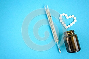 The heart made of tablets, medical thermometer on blue background