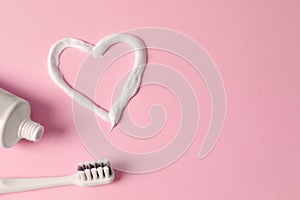 Heart made with toothpaste, tube and brush on pink background, flat lay. Space for text