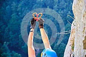 Heart made of two carabiners shining in the sun, held up by a woman climber on the via ferrata route in Vadu Crisului