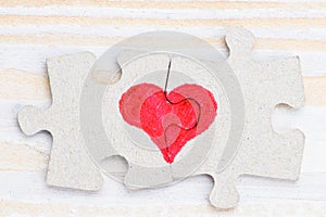 Heart made of two pieces of jigsaw puzzle on light wooden table, close-up