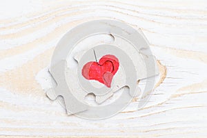 Heart made of two pieces of jigsaw puzzle on light wooden table, close-up