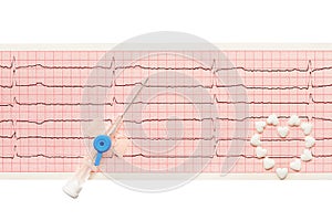 Heart made of white heart shape tablets and blue plastic catheter with open needle on paper ECG results