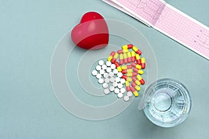 Heart, medical pills, cardiogram, glass of water, capsules on gray background.