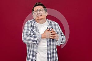 Heart pain attack or infarct. Portrait of middle aged man in casual checkered shirt and eyeglasses standing and holding his