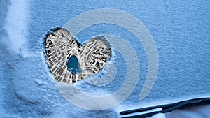 Heart painted on the snow-covered windshield of a car. Winter lovestory