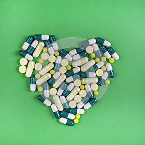 Heart of pills and capsules on green background