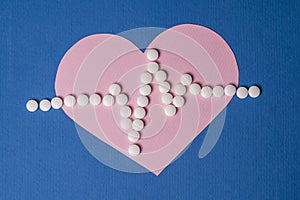 Heart pulse is lined with small white pills on a paper pink heart background.
