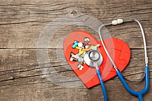 Heart puzzle red and color pills and stethoscope on a wooden background background. Concept treatment of heart disease pills