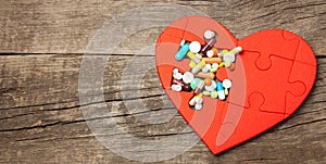 Heart puzzle red and colored pills and capsules on wood background. Concept treatment of heart disease pills. Copy space for text