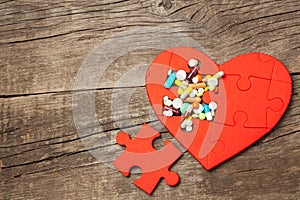 Heart puzzle red and colored pills and capsules on wood background. Concept treatment of heart disease pills. Copy space for text
