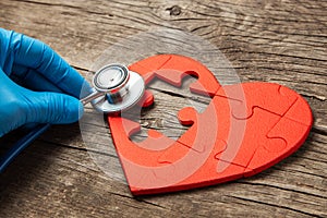 Heart puzzle red and stethoscope on wooden background. Concept diagnosis and treatment of heart disease, medical insurance
