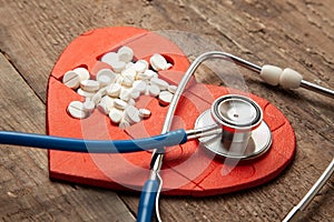 Heart puzzle red and white pills and a stethoscope on a wooden background background. Concept treatment of heart disease pills