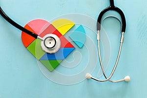 Heart puzzle and with stethoscope on blue pastel wooden background, medical concept