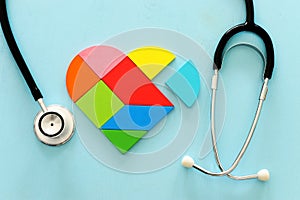 Heart puzzle and with stethoscope on blue pastel wooden background, medical concept