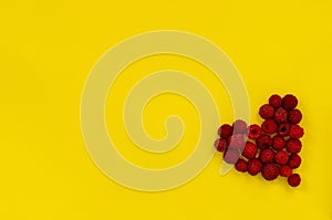 Heart of raspberries on yellow background. Colorful diet and healthy food concept. Background of raspberries. Top view. Copy space