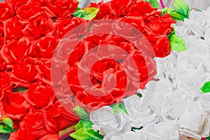 Heart of red artificial roses opposite white inanimate background flowers