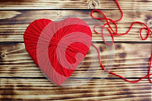 Heart of red color with thread lies on a wooden background