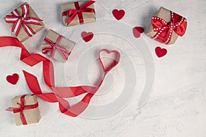 Heart from a red ribbon, gifts with a red ribbon and red hearts on a white stone background. Valentine`s day background. Valentin