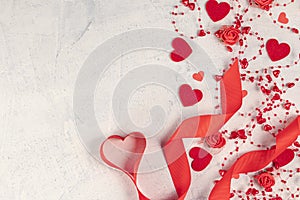 Heart from a red ribbon, red hearts, and beads with hearts on a white stone background. Valentine`s day background. Valentine`s
