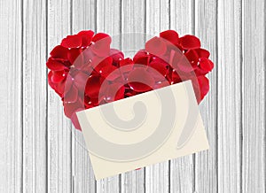 Heart from red rose petals and paper on wooden table