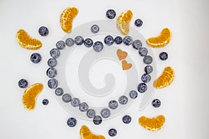 A heart`s frame from mandarin pieces and blueberry on white background. A composition of the mandarin pieces and berries in form