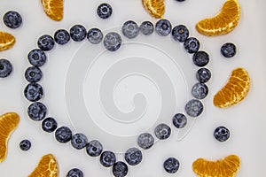 A heart`s frame from mandarin pieces and blueberry on white background. A composition of the mandarin pieces and berries in form