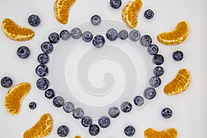 A heart`s frame from mandarin pieces and blueberry on white background. A composition of the mandarin pieces and berries in form