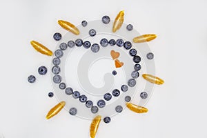 A heart`s frame from mandarin pieces and blueberry on white background. A composition of the mandarin pieces and berries in form