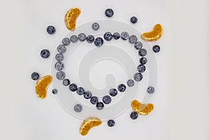 A heart`s frame from mandarin pieces and blueberry on white background. A composition of the mandarin pieces and berries in form