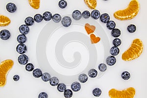 A heart`s frame from mandarin pieces and blueberry on white background. A composition of the mandarin pieces and berries in form