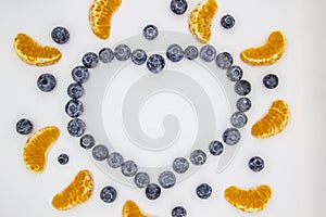 A heart`s frame from mandarin pieces and blueberry on white background. A composition of the mandarin pieces and berries in form