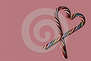 Heart shape with Christmas candy canes on pink background, top view, copy space. Can be used as greeting cards