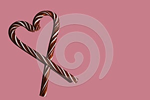 Heart shape with Christmas candy canes on pink background, top view, copy space, minimalism