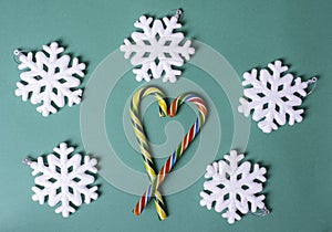 Heart shape with Christmas candy canes, white large snowflakes on a green background, top view