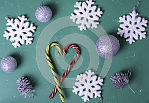 Heart shape with Christmas candy canes, white large snowflakes, silvery balls on a green background, top view