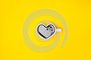 Heart shape coffee cup over yellow background. View from above.