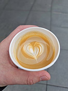 Heart shape on coffee foam. Take away coffee macchiato holds a hand.