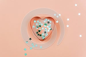 Heart shape cookie cutter and blue confetti on coral pink background. Valentines day concept. Top view, flat lay