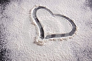 A heart shape drawn on flour on a black background. Close-up